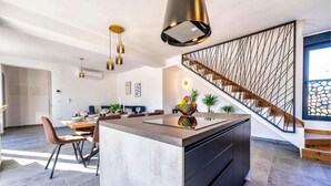 A modern kitchen with a central island, pendant lighting, and a staircase with a geometric railing. - Luxurious home in Zadar (Zadar)