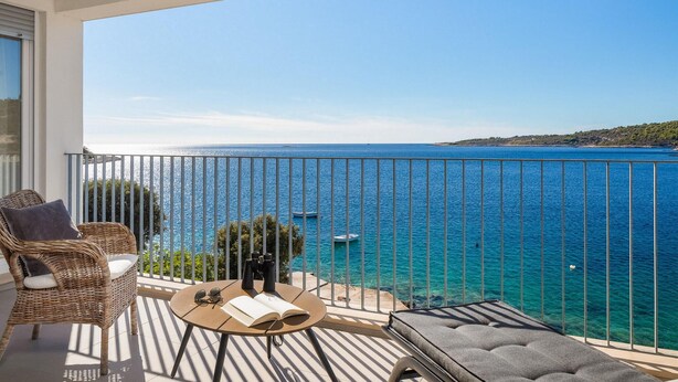 Un balcon avec vue sur la mer, des meubles en osier et une table avec des jumelles et un livre.
