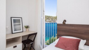 Une chambre à coucher avec un lit, un bureau, une chaise, une fenêtre donnant sur la mer et une petite plante.
