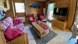 Una cabaña de madera acogedora con sofá, dos sillones, una mesa de centro, televisor y un cuadro en la pared.