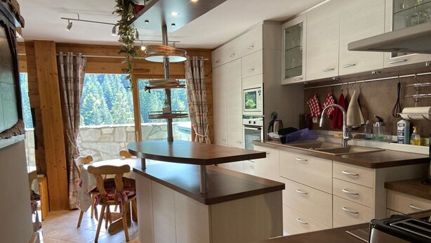 Una cocina moderna con una isla central, armarios blancos y vistas al exterior a través de amplios ventanales.