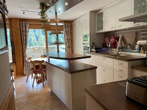 A modern kitchen with a central island, white cabinetry, and a view of the outdoors through large windows.