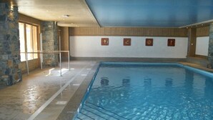 Una piscina interior con paredes de piedra, suelo de baldosas y techo de madera.