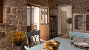 Interior rústic de pedra amb una taula de dinar preparada per a un àpat, una porta de fusta que dona a una altra estança i un armari amb portes de vidre.