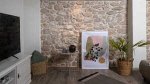 Un saló amb una paret de pedra, un quadre abstracte emmarcat, una taula petita amb un ram i una televisió sobre un moble.