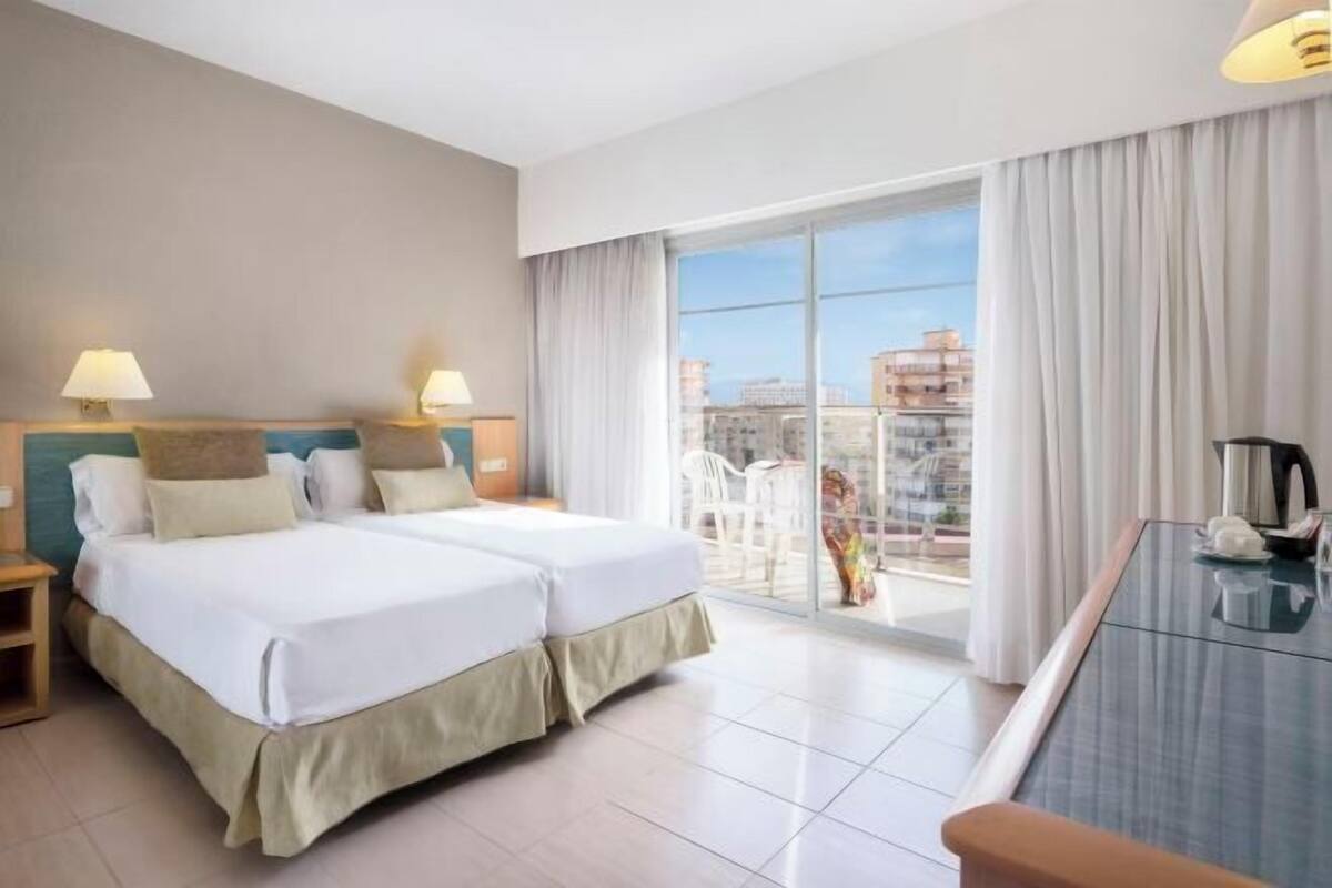 A hotel room with two beds, a balcony with a view, and a dining table.