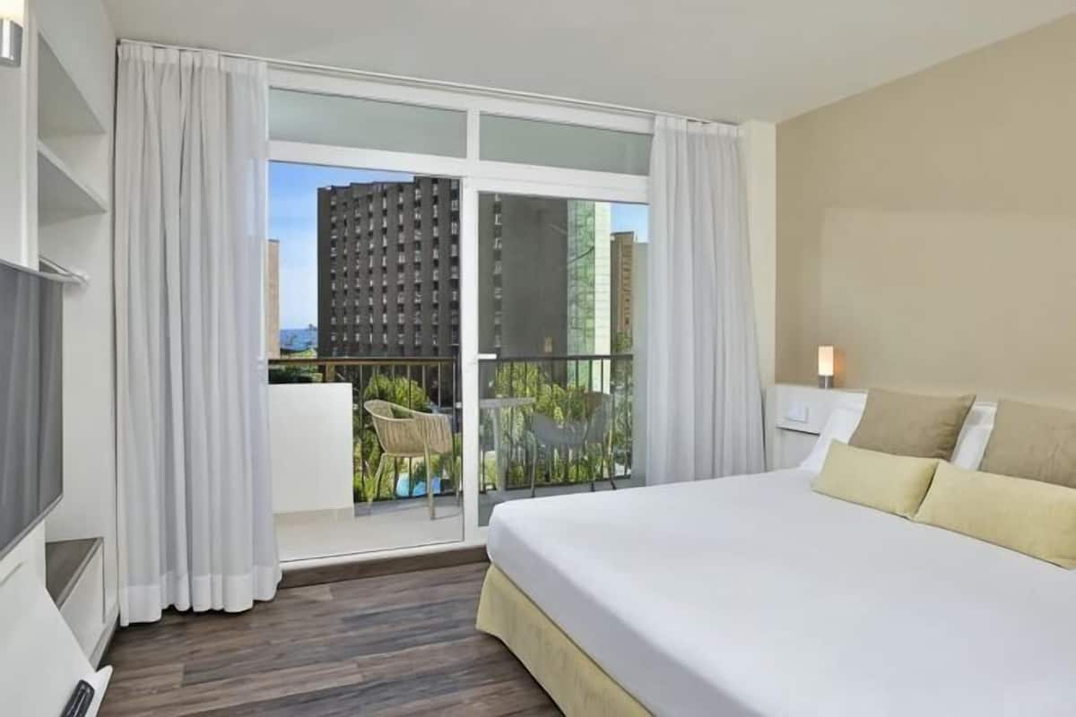 A hotel room with a bed, a TV, a balcony with a table and chairs, and a city view.