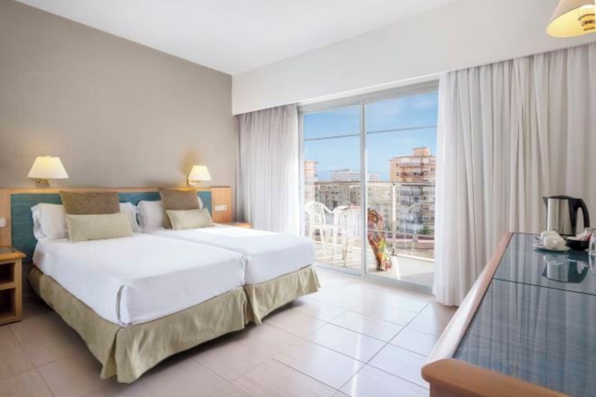 A hotel room with two beds, a balcony with a view, and a dining table.