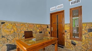 A stone-walled room with a wooden table and a laptop, a wooden door, and a window with a view.