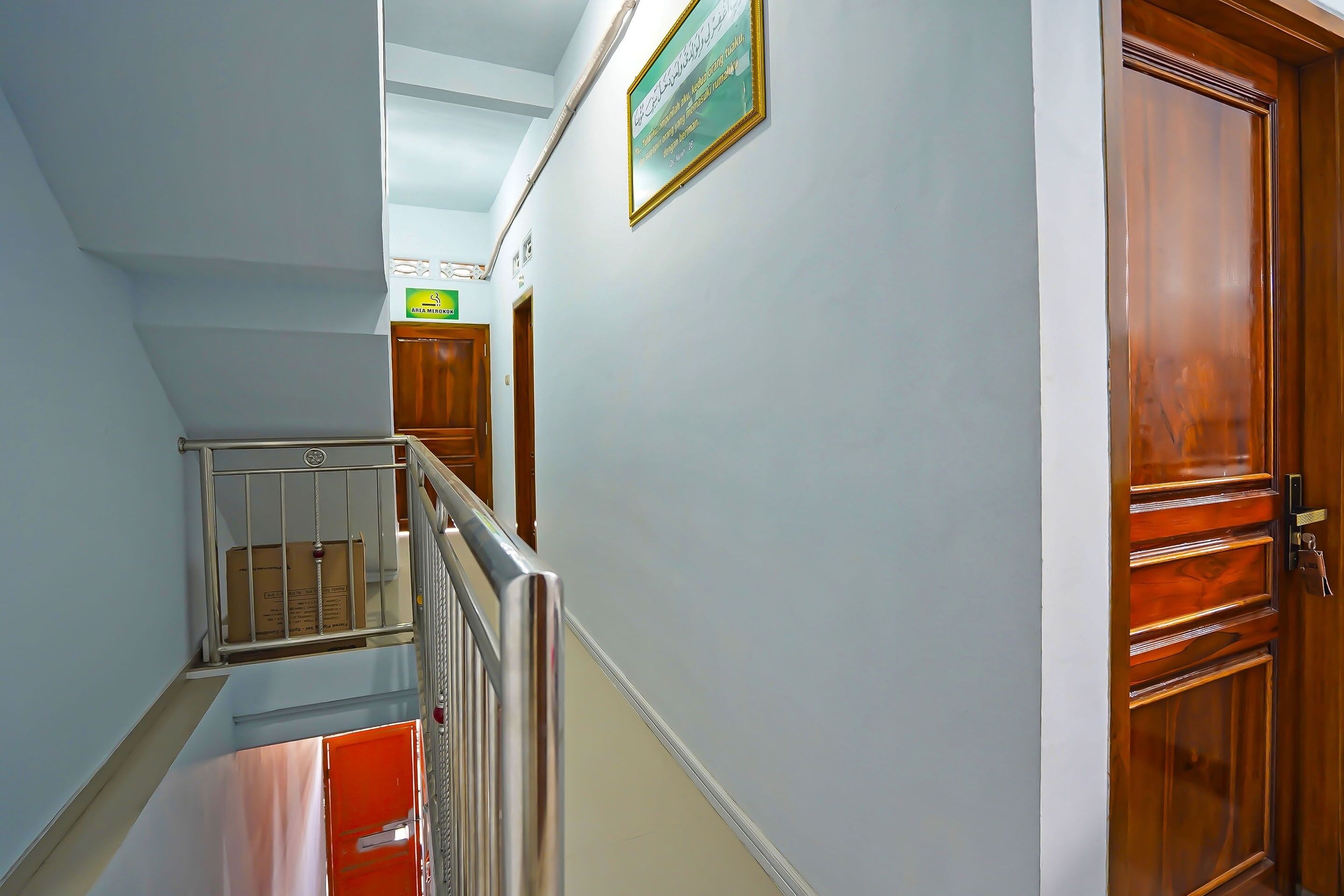 Un pasillo con una escalera, una puerta de madera y un cartel enmarcado en la pared.