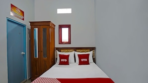 A hotel room with a blue door, a wooden wardrobe, a bed with red and white bedding, and a small window.