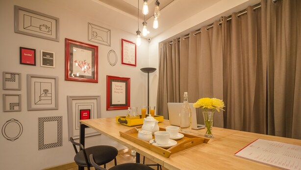 A modern dining area with a wooden table, black chairs, a tray with white cups and a teapot, and a vase with yellow flowers.