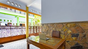 A room with a wooden desk, a laptop, a stone wall, and a balcony with a view of greenery.