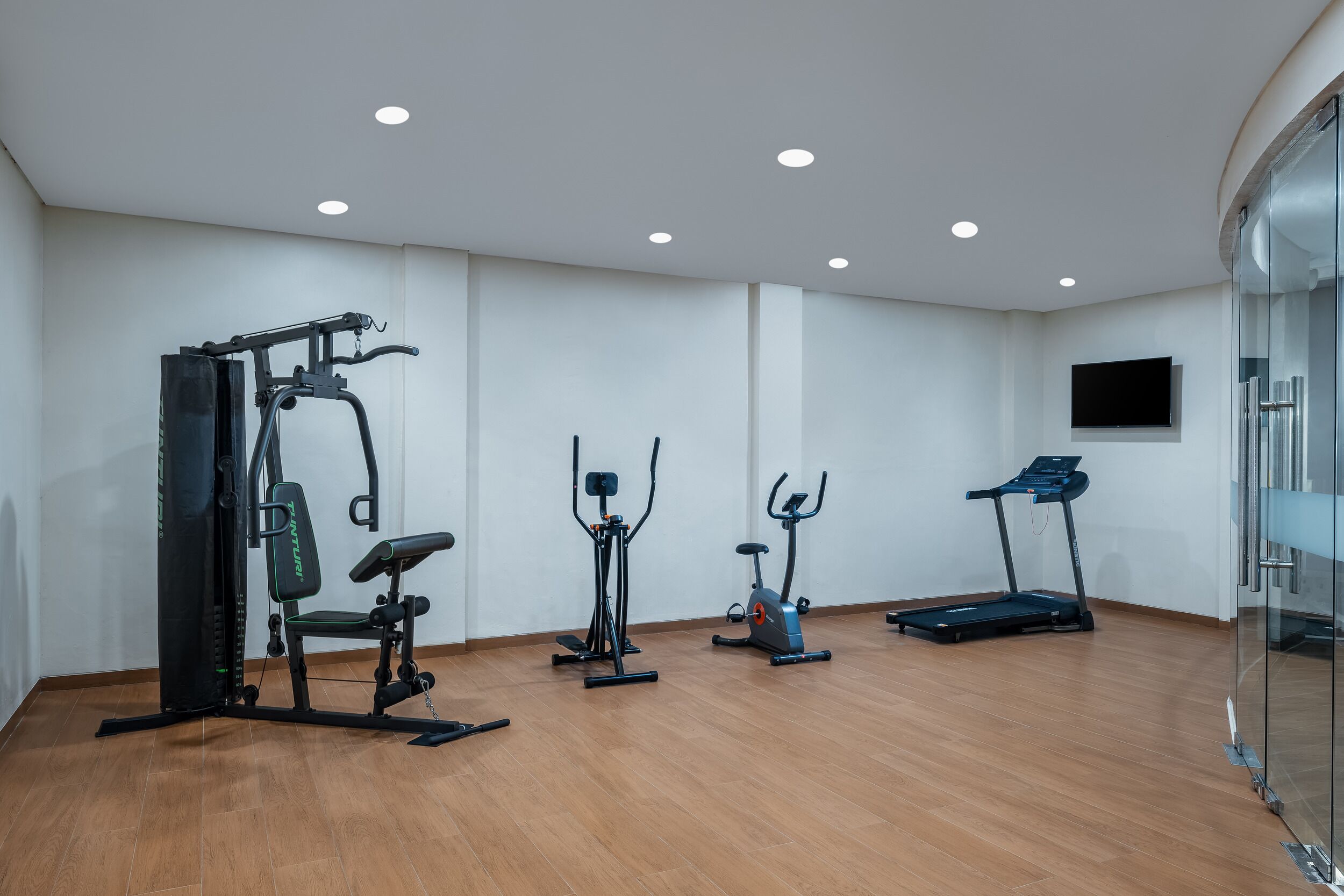 A gym with various exercise equipment, a treadmill, and a television on the wall.