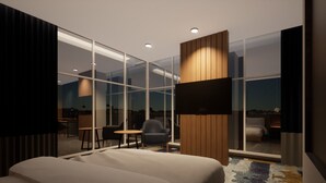 A modern hotel room with a large bed, a seating area with a table and chairs, and a view through floor-to-ceiling windows.