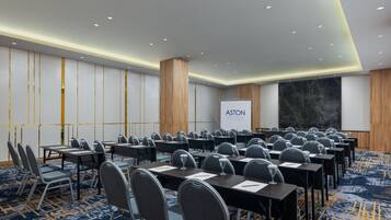 A conference room with rows of tables and chairs, a large screen, and a marble wall.