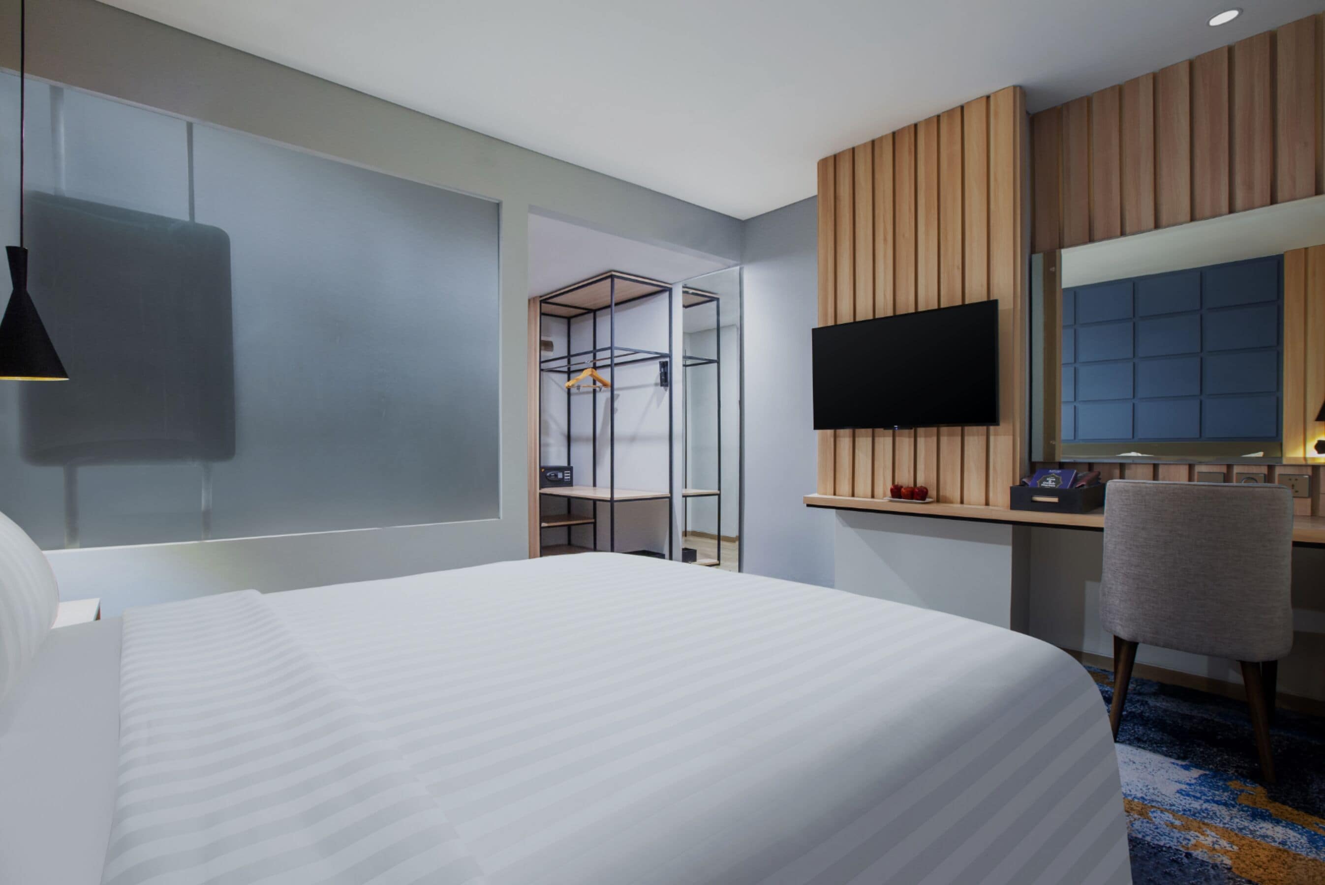 Une chambre d’hôtel moderne dotée d’un grand lit, d’un bureau avec un téléviseur à écran plat, d’une chaise et d’une armoire avec un miroir.