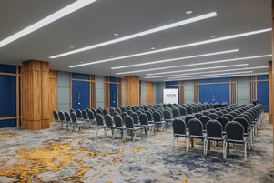Un salón de conferencias con hileras de sillas, paneles de madera y una pared azul de acento.