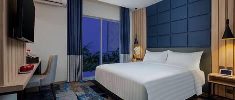Quarto de hotel com uma cama grande, uma escrivaninha com cadeira, televisão e janela com cortinas.