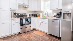 A modern kitchen with white cabinets, stainless steel appliances, and a wooden floor.