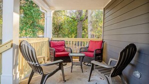 A covered porch with wicker furniture and red cushions, overlooking a wooded area.