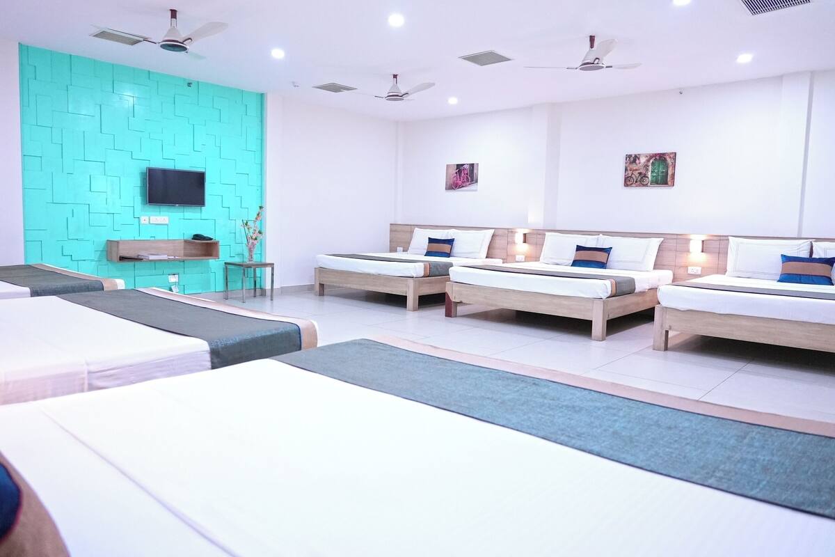 A hotel room with three beds, a TV, ceiling fans, and artwork on the walls.