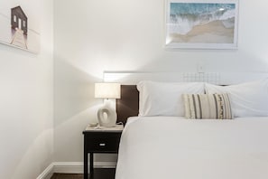 Ein Hotelzimmer mit einem Bett, einem Nachttisch mit Lampe, einem gerahmten Bild an der Wand und einem kleinen Tisch mit einer Schale.