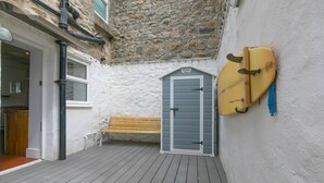 A narrow wooden deck with a stone wall, a bench, and surfboards mounted on the wall. - Floyd’s, St Ives – Sleeps 8 – Dog Friendly – Off-Site Parking (St Ives)