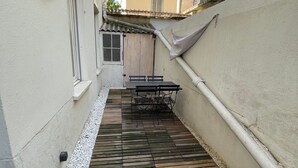 A narrow courtyard with a wooden deck and a table with chairs. - Appartement au Cœur du Centre Ville - T3 (Perpignan)