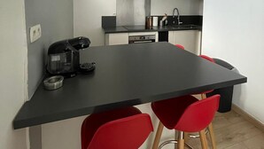 A compact kitchen with a black countertop, stainless steel appliances, and red bar stools. - Appartement au Cœur du Centre Ville - T3 (Perpignan)