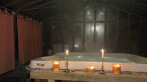 Een gedimde kamer met een houten tafel waarop kaarsen en glaasjes staan, een whirlpool achtergrond en een rustieke houten vloer.
