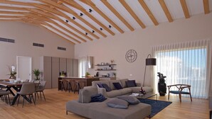 A spacious living area with a wooden ceiling, a sofa, a dining table, and a kitchen in the background.