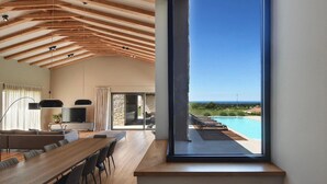 A modern interior with a dining area, a TV, and a view of a pool and landscape.