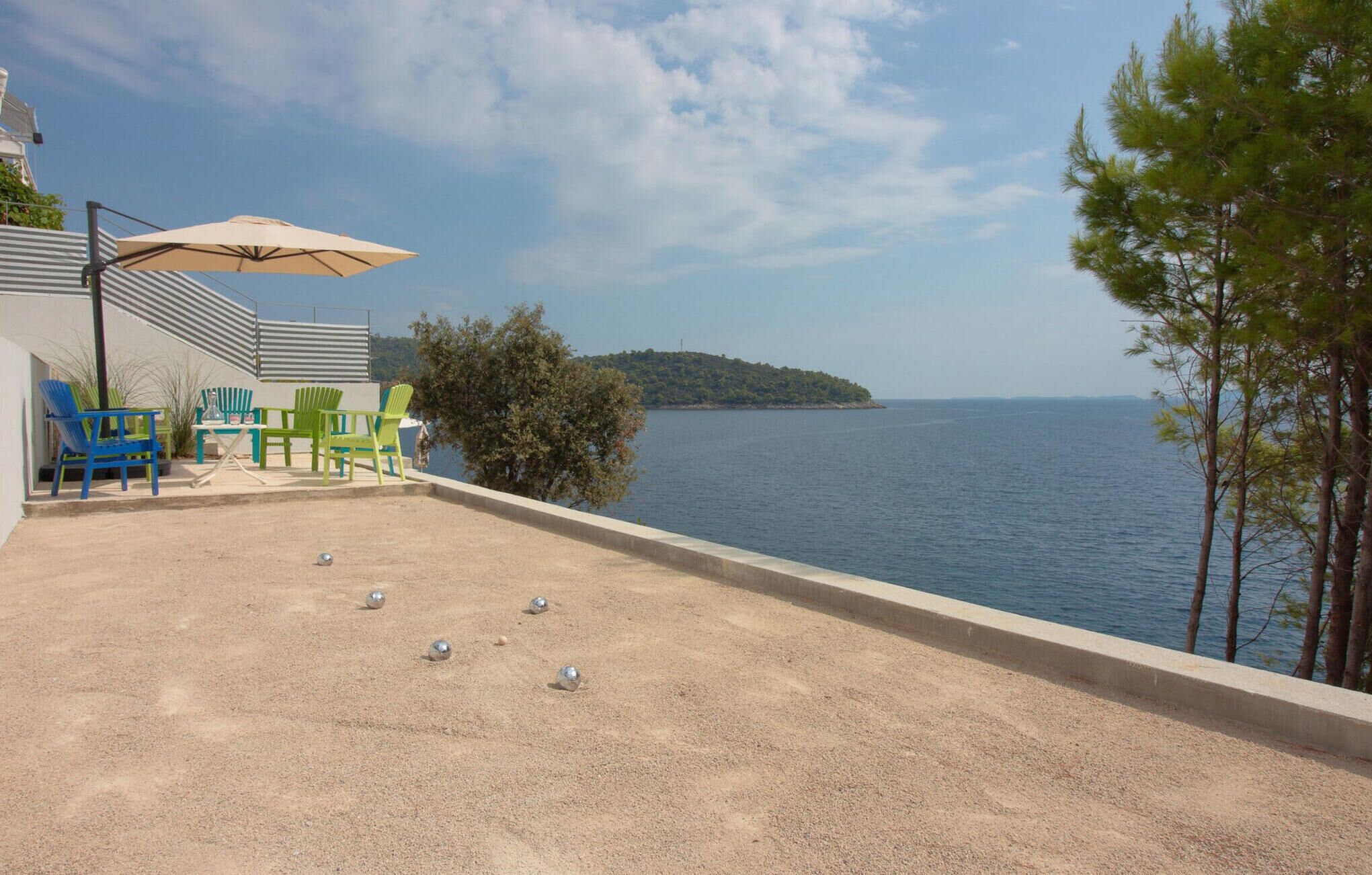 Un área de piscina con vista al mar, un espacio de descanso con sillones y un edificio con techo inclinado.
