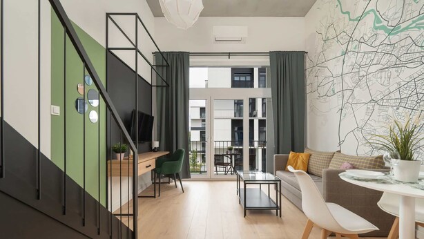 Un intérieur moderne avec un escalier, un coin repas et une vue sur un immeuble à travers de grandes fenêtres.