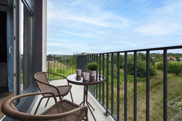 A balcony with wicker chairs, a small round table, and potted plants.