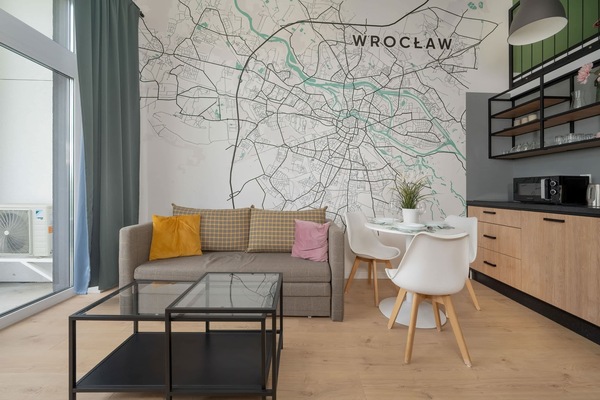 A stylish studio apartment with green accent walls, modern furniture, and a cozy seating area with a small dining table.