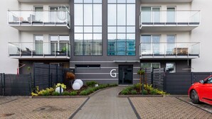Un edificio moderno de dos pisos con entrada central, ventanas amplias y un camino de acceso con portón.