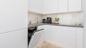 Una cocina moderna con armarios blancos, lavavajillas, cafetera y una planta en maceta.