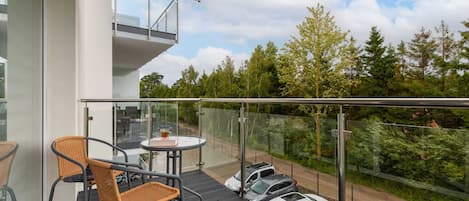 A balcony with a glass railing, a table, chairs, and parked cars.