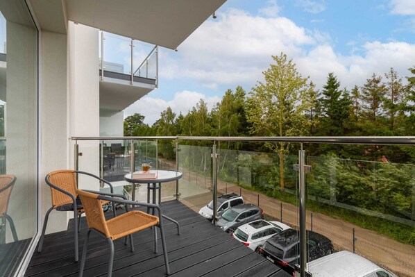 A balcony with a glass railing, a table, chairs, and parked cars.