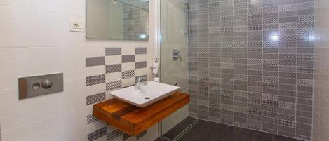A modern bathroom with a glass shower enclosure, a white sink with a wooden countertop, and patterned tiles on the walls.