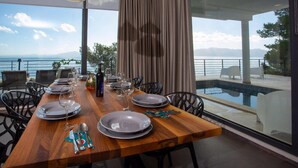 A dining table set for six with plates, glasses, and cutlery, overlooking a pool and a scenic view.