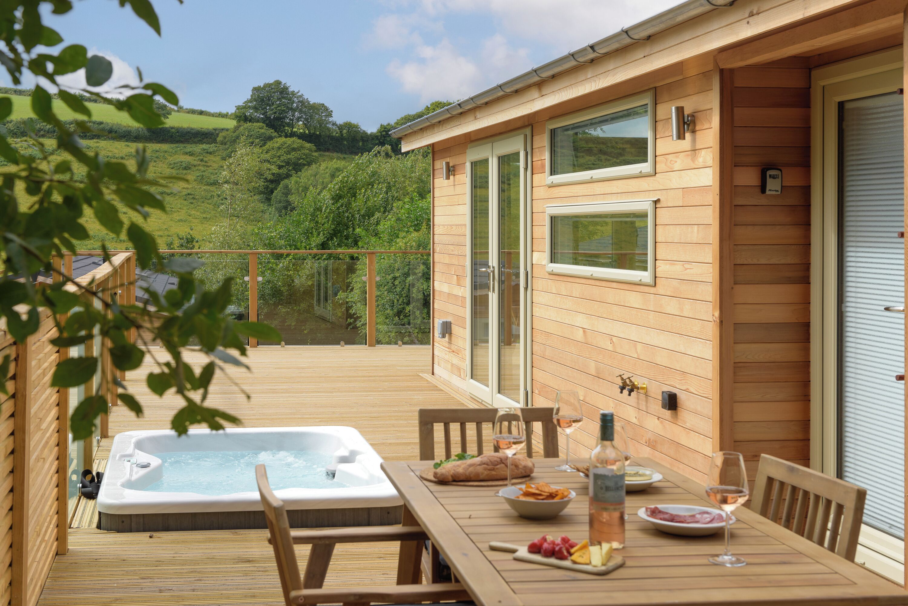 Eine Holzterrasse mit Whirlpool, Esstisch und Stühlen sowie Blick auf die Landschaft.
