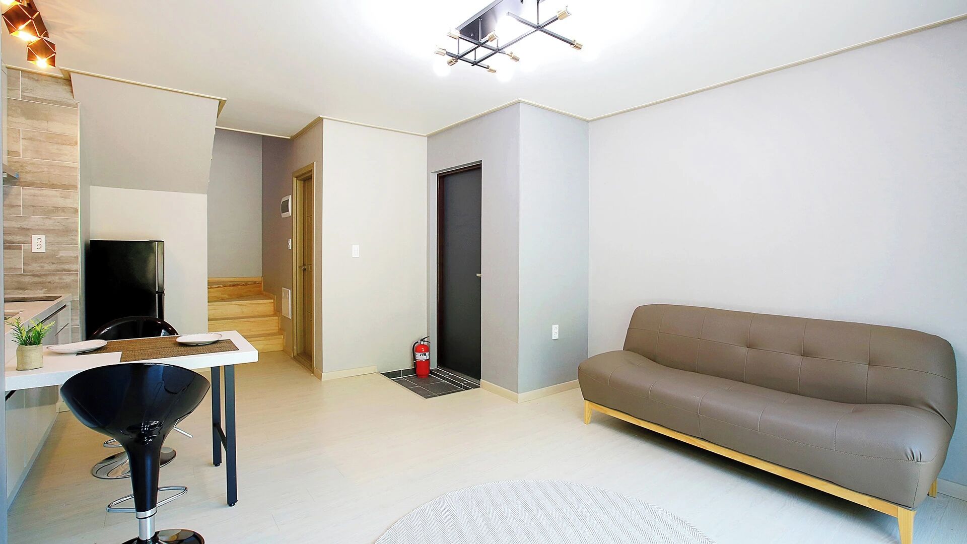Una sala de estar moderna con un sofá, una mesa de comedor con sillas, una cocina y una escalera.