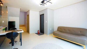 A modern living room with a sofa, a dining area with a table and chairs, a kitchen area with a fridge, and a staircase leading to another room. - Hongcheon Stone Brown Pension (Hongcheon)