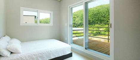 A bedroom with a bed, a window, and a view of a balcony.