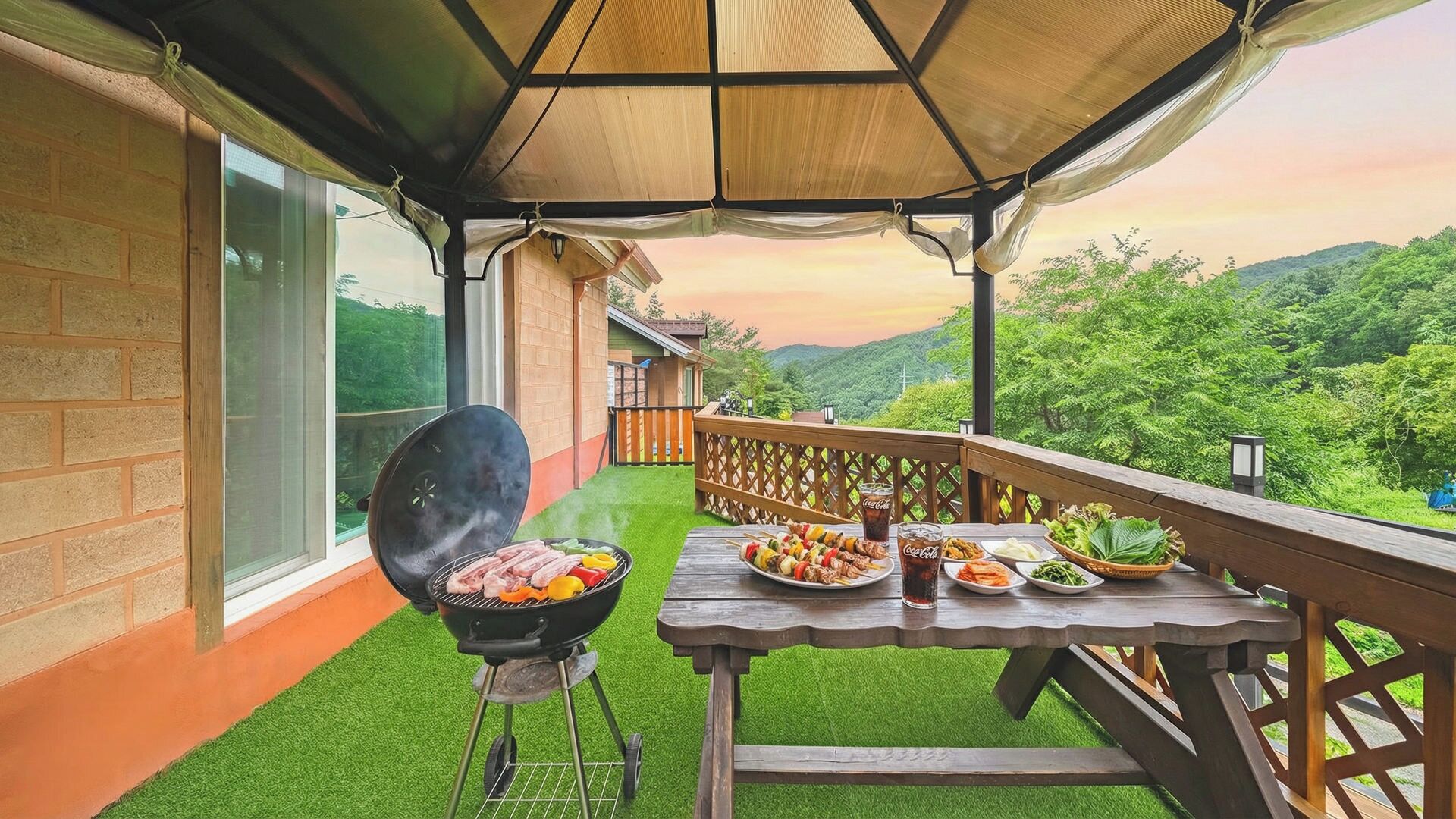 An outdoor patio with a barbecue grill, dining table, and a view of a lush green landscape.