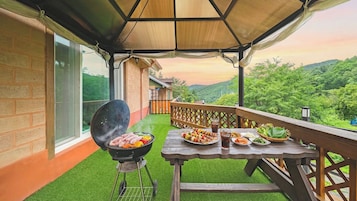 Un patio al aire libre con una parrilla, mesa de comedor y vistas a un paisaje verde y exuberante.