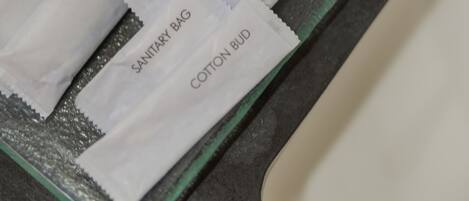 Ein Badezimmer-Waschtisch mit einer Glasablage, auf der verschiedene Pflegeprodukte liegen, darunter eine Hygiene-Tasche, Wattestäbchen, Seife und Duschcreme.